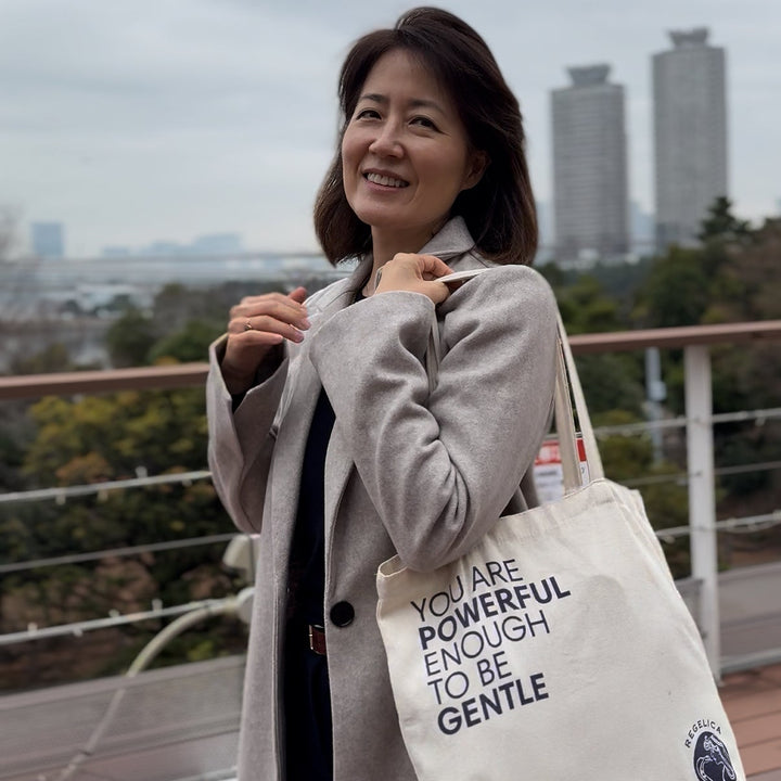 Woman holding a tote bag with a motivational quote against an urban skyline.
